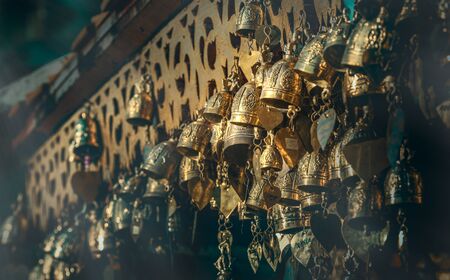 Many small shinning brass bells hanging on temple roof. Faith of Buddhism in Thailand. Adjusted colour and tone, selected focus, blur background and foreground.の写真素材