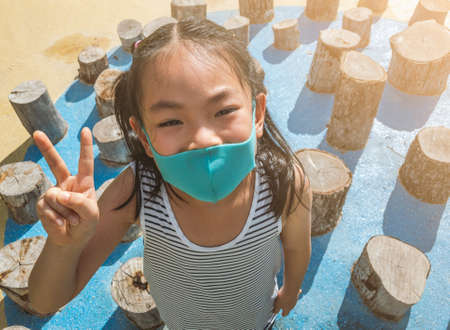 Top view Asian little girl in outdoors activity, wearing protective mask. Standing on balance toys...