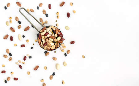 Isolated varieties of beans in stainless steel measuring cup on white background, some beans spread outside. Top view image mix beans, flat lay design with space for text.の写真素材