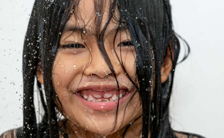 Close up cute face of Asian child girl, happy face under shower rain on white background, big smile on face, wet and water drop on skin.の写真素材