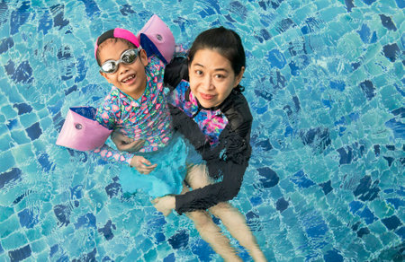 Beautiful Asian mother playing with daughter in swimming pool, view from above. Asian middle-aged...