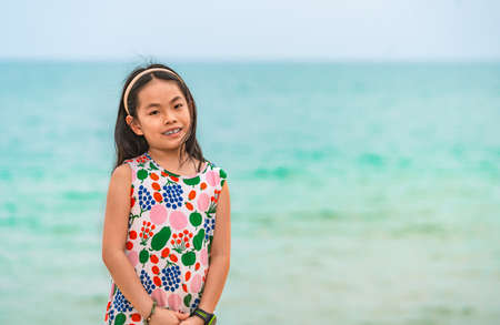 Portrait Asian little child girl on a beach, background of blurred sea and sky. Child girl with long black hair, smile, eyes looking at camera, blank space for copy and design.の写真素材