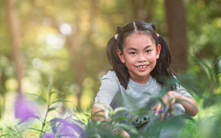 Portrait of healthy Asian little girl posing in a garden in public park in a morning, smiling face with little bit sweat on her face, blank space for text and design.の写真素材