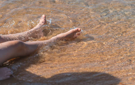 Close up child's legs relaxing in sea water on the beach, sunny day light in a morning, blank space for text and design.の写真素材