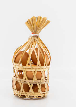 Isolated organic brown chicken eggs in round bamboo wicker basket on white background, front view...