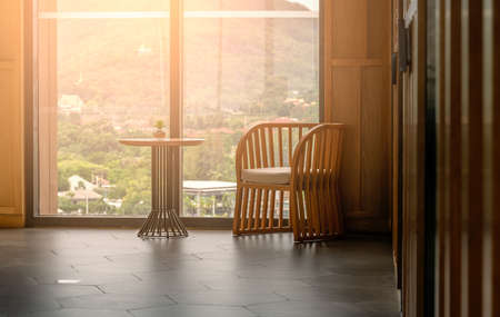 One relaxes chair and a small desk with small glass pot of plant in a building, background of big...