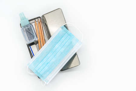 Top view stainless steel pencil box with pencils, medical face mask and a small bottle of alcohol,...