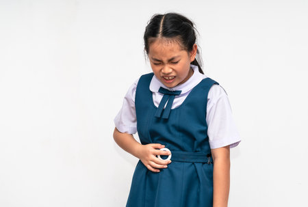 Little Asian student girl is stomach ache, unidentified school uniform, isolated portrait of Asian...