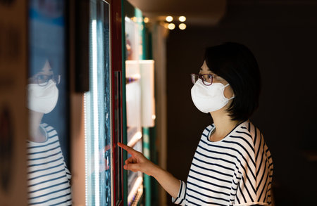 Profile portrait of middle-aged Asian woman buying drinks or other products from a vending machine,...