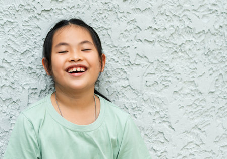 Portrait healthy Asian child girl with happiness mood, standing at the textured white wall, cute face with smiling and laughing, black hall hair, empty space for copy and design.の写真素材