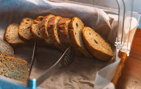 Sliced wholegrain bread in basket on dark-brown rustic wooden table, natural light from window.