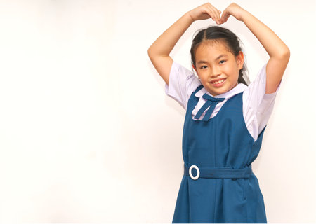 A cute portrait of an Asian student girl in uniform making a heart gesture by bending her arms into...