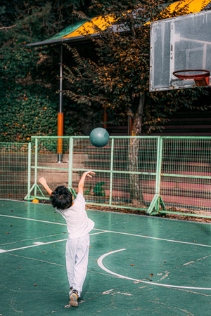 A young boy holding a green basketball and shooting at the goal. A moment. Back view.の写真素材