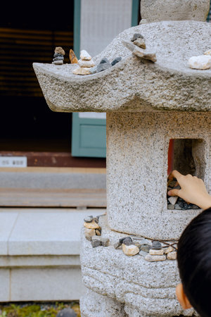 A child's hand stacking stones on a stone statue to make a wish.の写真素材