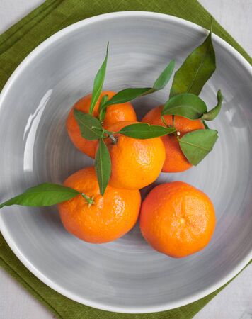 Clementine tangerines with green leaves on white wooden background in a grey bowl. Green fabricの写真素材