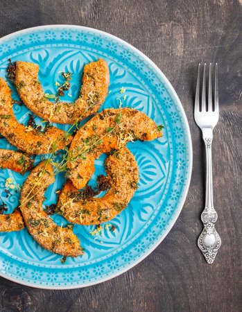Rustic style baked pumpkin slices with herbs on wooden table in a blue bowlの写真素材