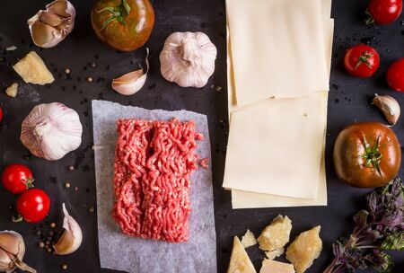 Set of ingredients for italian lasagne. Pasta, tomatoes, fresh ground meat, parmesan, mozzarella, basil, garlic on a rustic chalkboard. Overheadの写真素材