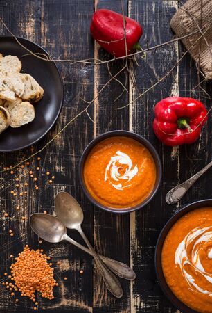 Delicious pumpkin soup with heavy cream on dark rustic wooden table with red bell pepper, bread toasts, lentil and autumn branches. Top viewの写真素材