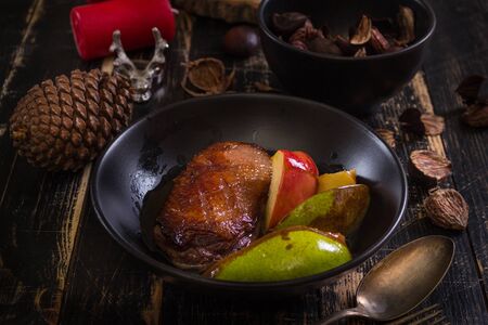 Roasted duck breast with golden crispy skin served with baked apples and chestnuts. Served on a ceramic black plate over rustic dark wooden table with a deer napkin ring and candles.の写真素材