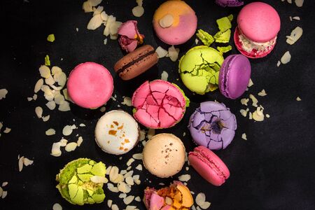 Assorted colorful french macarons and almond flakes on a black background. Closeup. Top view....