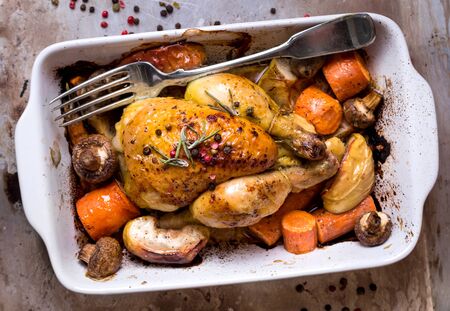 Whole baked juicy chicken with golden crispy skin. Roasted chicken in baking dish with apples, carrot, mushrooms, rosemary, garlic, pepper on rustic iron oven-tray. Overhead. Dinner. Cooked poultryの写真素材