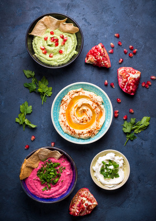 Colorful hummus bowls. Different kinds of dips. Traditional hummus, herbs hummus, beetroot hummus, spread. Assorted meze and dips with crispy pita. Meze and snacks concept. Middle eastern snacks setの写真素材