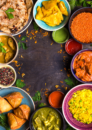 Assorted indian food on dark wooden background. Dishes of indian cuisine. Curry, butter chicken, rice, lentils, paneer, samosa, naan, chutney, spices. Space for text. Bowls and plates with indian foodの写真素材