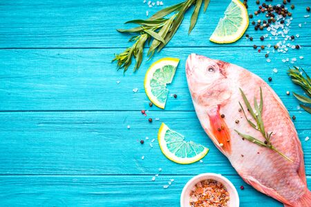 Fresh fish tilapia ready to cook. Raw fish with herbs, lemon, salt, pepper on wooden rustic...