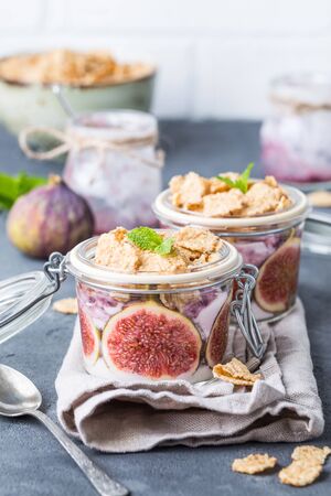 Homemade healthy yoghurt in glass pot with cereals, figs, mint on rustic concrete background. Healthy morning breakfast. Freshly made yoghurt with oat granola and fruit. Yoghurt in jar with muesliの写真素材