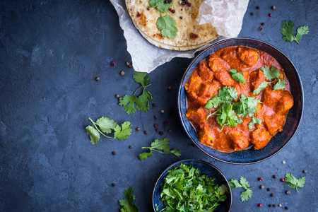 Traditional Indian/British dish chicken tikka masala background. Spicy chicken tikka masala/curry in bowl, indian bread naan, fresh cilantro. Indian style dinner. Space for text. Top view. Indian foodの写真素材