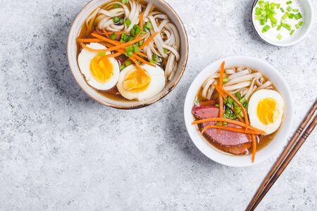 Bowls with Japanese soup ramen, chopsticks, white concrete rustic background. Traditional Asian soup with noodles, meat, broth, eggs. Asian food. Japanese ramen for dinner. Ramen, close-up. Overhead
の写真素材