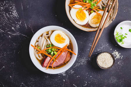 Bowls with Japanese soup ramen, chopsticks, black concrete rustic background. Traditional Asian soup with noodles, meat, broth, eggs. Asian food. Japanese ramen for dinner. Ramen, close-up. Overheadの写真素材