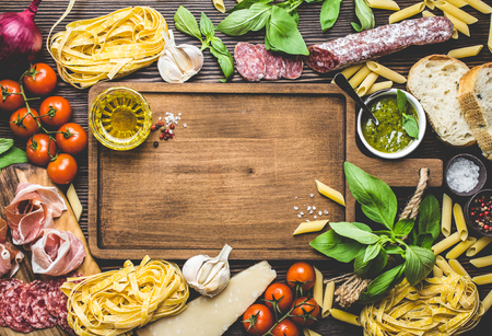 Top view of Italian traditional food, appetizers and snacks as salami, prosciutto, cheese, pesto, ciabatta, olive oil, pasta on rustic wooden board with space for text and retro styleの写真素材