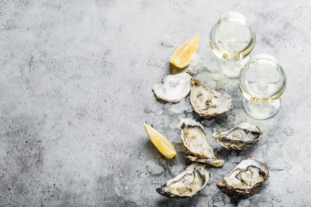 Close-up of half dozen of fresh opened oysters and shells with lemon wedges, two glasses of white wine or champagne, top view, grey rustic concrete background, space for text. Romantic or celebration
の写真素材