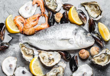 Fresh raw fish Dorado, oysters, shrimps, clams, mussels, shells with lemon on grey stone rustic background, top view, close-up. Assortment of fish and seafood, diet, healthy eatingの写真素材