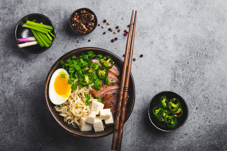 Delicious Asian noodle soup ramen in bowl with meat broth, tofu, sliced pork, egg with yolk, grey rustic concreteの写真素材