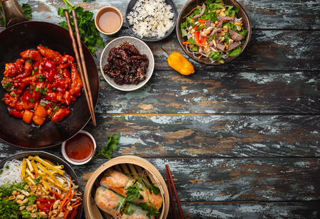 Set of assorted Chinese dishes on table: sweet and sour chicken in wok pan, dim sum, spring rolls, noodles, salad, rice, steamed buns. Asian style dinner or buffet with top view and space for text
の写真素材
