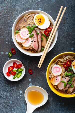 Cooking Japanese noodle soup ramen. Ramen with sliced pork, narutomaki, egg and kitchen spoon with broth on rustic stone background. Making traditional dish of Japan, top view, close-up, conceptの写真素材