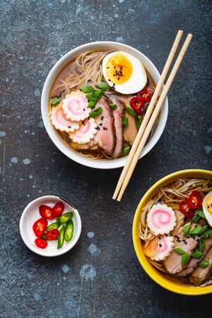 Two bowls of Japanese noodle soup ramen with meat broth, sliced pork, narutomaki, egg with yolk on rustic stone background. Traditional dish of Japan, top view, close-up, conceptの写真素材