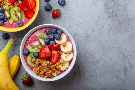 Summer acai smoothie bowls with strawberries, banana, blueberries, kiwi fruit and granola on gray concrete background. Breakfast bowl with fruit and cereal, close-up, top view, space for textの写真素材
