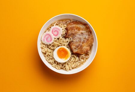 Top view of Japanese noodle soup ramen in white bowl with noodles, meat broth, sliced roasted pork, narutomaki, egg with yolk on bright orange background. Traditional dish of Japan, close-up.の写真素材