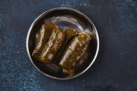 Traditional Middle Eastern dish Dolma in vine leaves in rustic metal plate on blue rustic background top view. Arab meze for snack or lunch, Middle Eastern cuisine .の写真素材