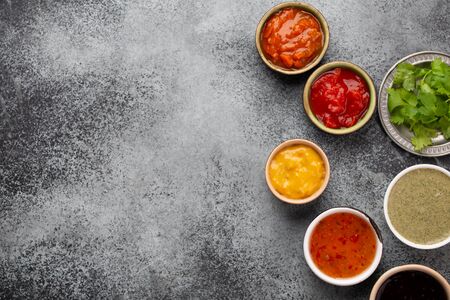 Assorted Indian chutneys in small rustic bowls on grey concrete background. Top view of colorful...