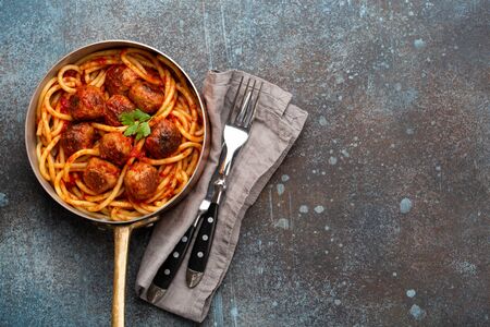 Overhead of traditional homemade pasta with roasted meatballs, tomato sauce in copper vintage pan on rustic concrete background. Classic homemade meatballs spaghetti for dinner, space for textの写真素材