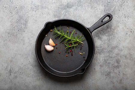 Black cast iron frying pan with rosemary, garlic, pepper top viewの写真素材