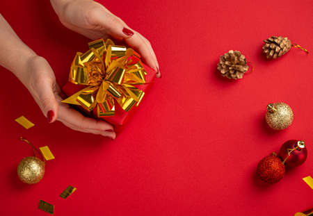 Female hands holding red and golden Christmas present top viewの写真素材