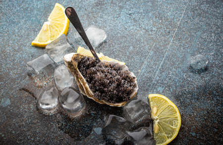 Black caviar served in oyster shell with spoon with lemon wedges and ice cubesの写真素材