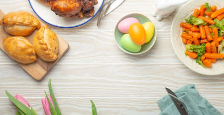 Easter food on white rustic table: pastel colored eggs, roasted chicken, vegetables