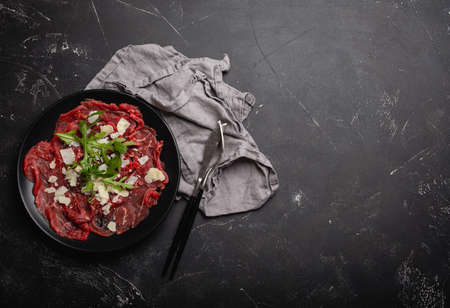 Cold meat appetizer Beef carpaccio with parmesan cheese and arugula on black plateの写真素材