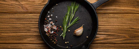 Black cast iron frying pan skillet with food cooking ingredients fresh rosemary, garlic, salt and pepperの写真素材